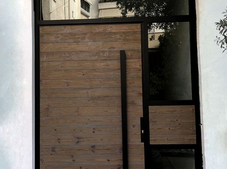 Πόρτα εισόδου κτηρίου με μεταλλικό σκελετό, γυαλιά διάφανα και διπλή επένδυση του κινούμενου φύλλου με ξυλεία πεύκης thermoWood.